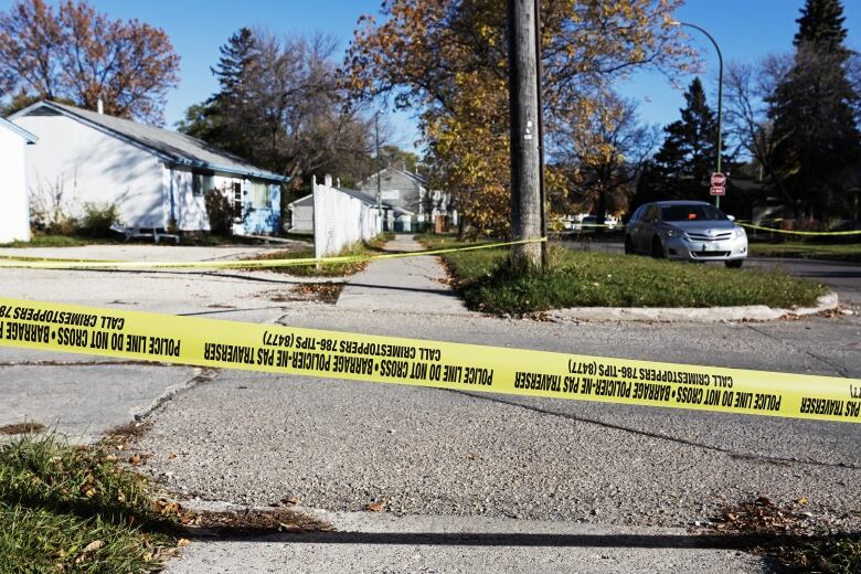 Yellow police tape is attached to a pole next to a side walk.