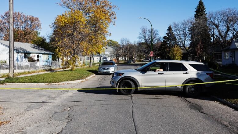 A grey vehicle sits across a road behind yellow police tape.