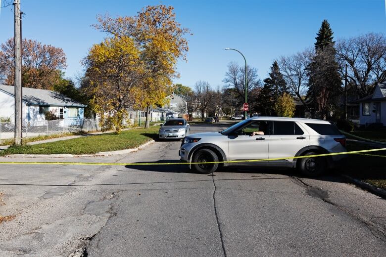 A grey vehicle sits across a road behind yellow police tape.