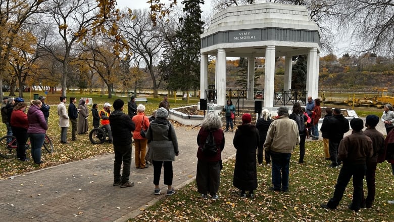 Many people are standing with their backs turned to the camera while someone is speaking into a microphone