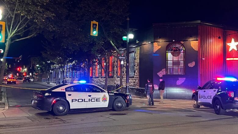 Hamilton police officers stand near police tape and two police cars outside a Hamilton nightclub where two men were shot.