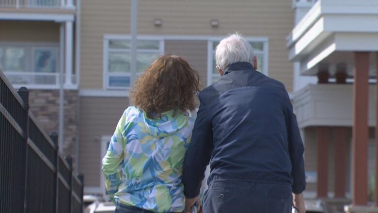 A woman and a man are seen from behind. They are walking toward a building. 