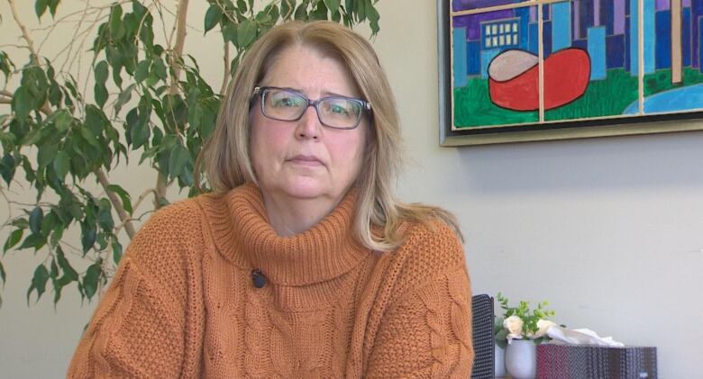 A woman in an orange turtleneck looks at the camera. 