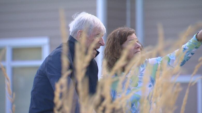 A woman points out something unseen for an older man. They are obscured by some wheat. 