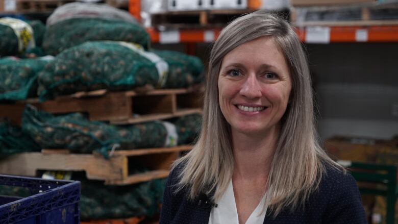 A woman smiles at the camera. She is sitting inside a warehouse buildling with crates in the background