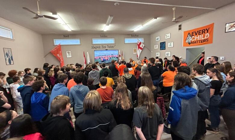 A room packed with people, many wearing orange.