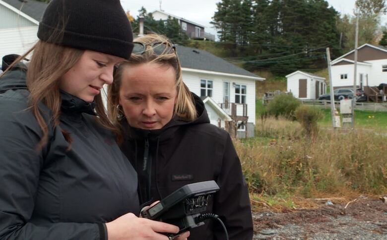 Two women look at a monitor screen while standing on a beach. 