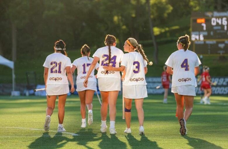 Female lax players pat each other on the back, on the field in the sunset.