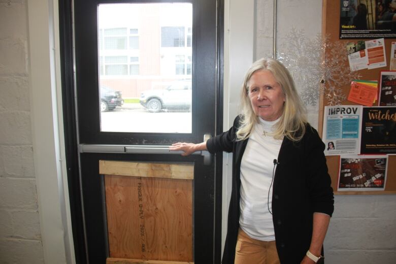 A woman stands near a boarded-up door