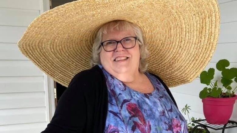 An older woman wearing a large straw hat smiles at the camera.