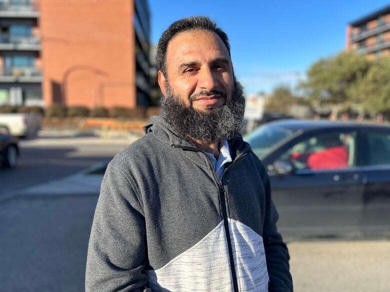 A man with a beard is standing in a parking lot. A street under construction can be seen behind him.