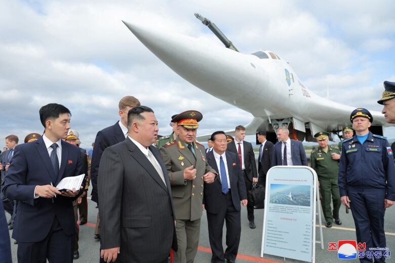 Men in suits and military uniforms inspect air bombers.