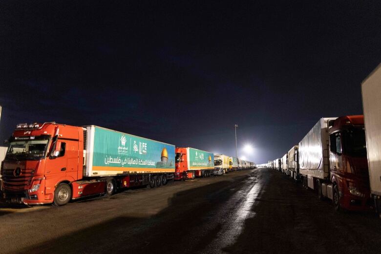 Parked tractor-trailers, part of a humanitarian aid convoy, line both sides of a road at on the Egypt side of border crossing with Rafah, Gaza.