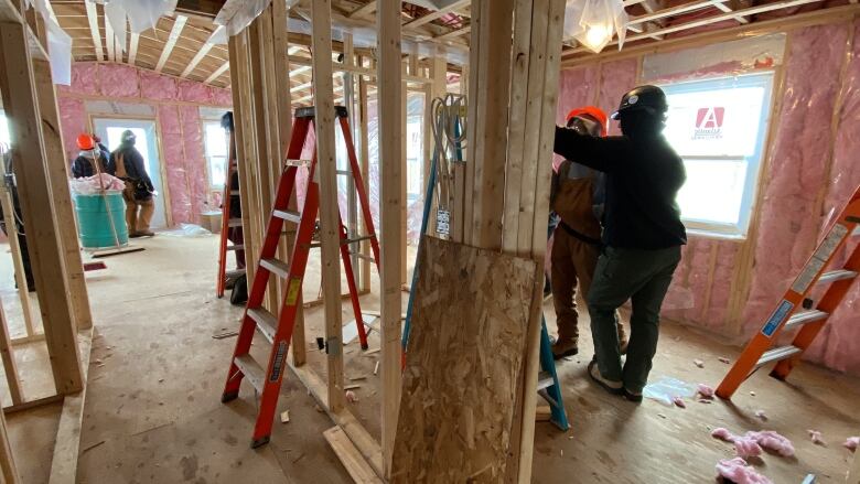 Several people at work inside a building under construction. Interior walls are studs only, and exterior walls show uncovered insulation.