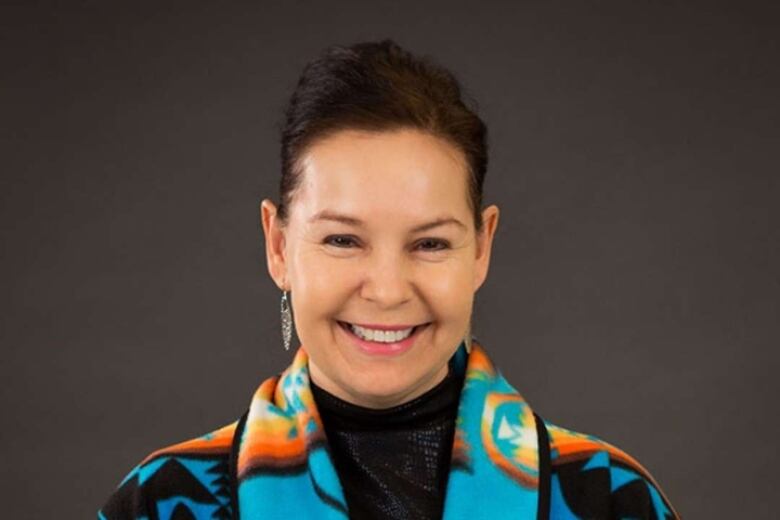 A portrait of a woman with dark hair, smiling, wearing a colourful coat.