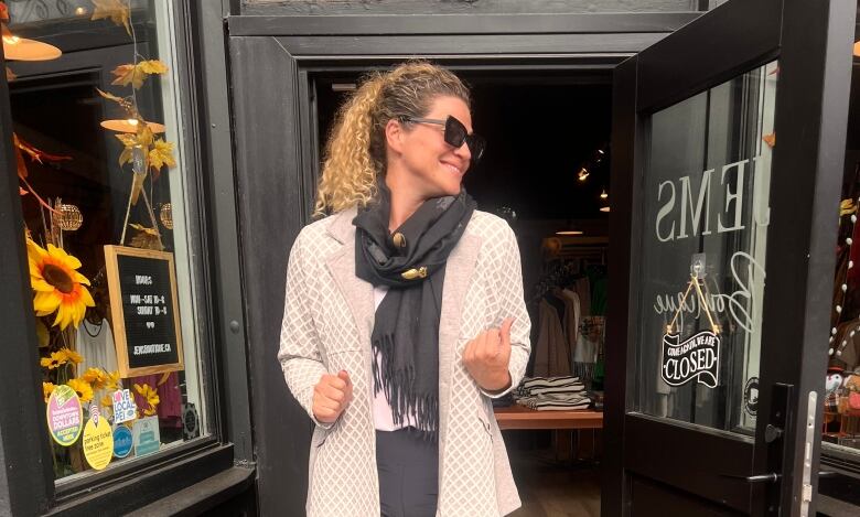 A woman stands in front of her store. 