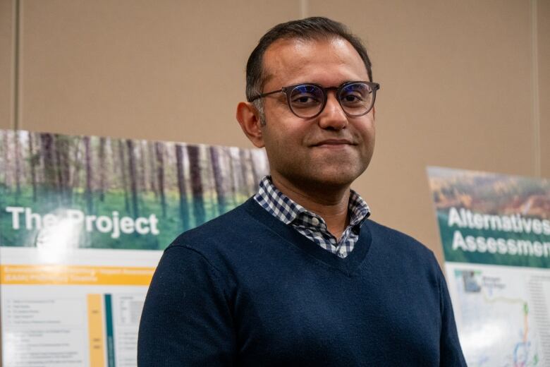 A man wearing a dark blue sweater stands in front of posters.