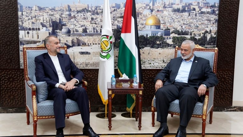 Two men sit in chairs with flags propped between them.