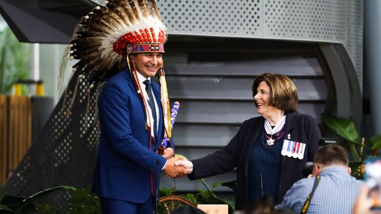 A mean wearing a headdress shakes hands with a woman.