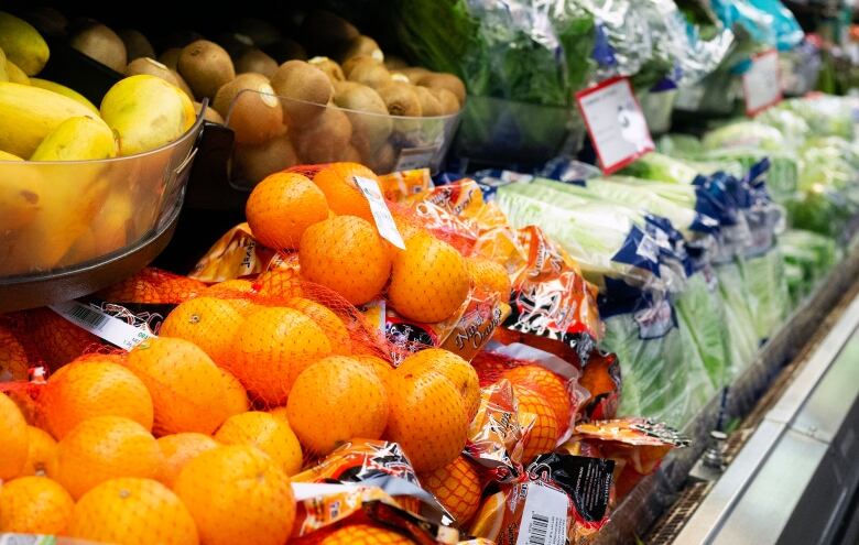 A view of produce on grocery store shelves, with bags of oranges in the foreground, and bags of lettuce further along the aisle.