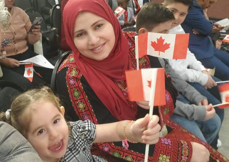 A woman and children sit together waving miniature Canadian flags