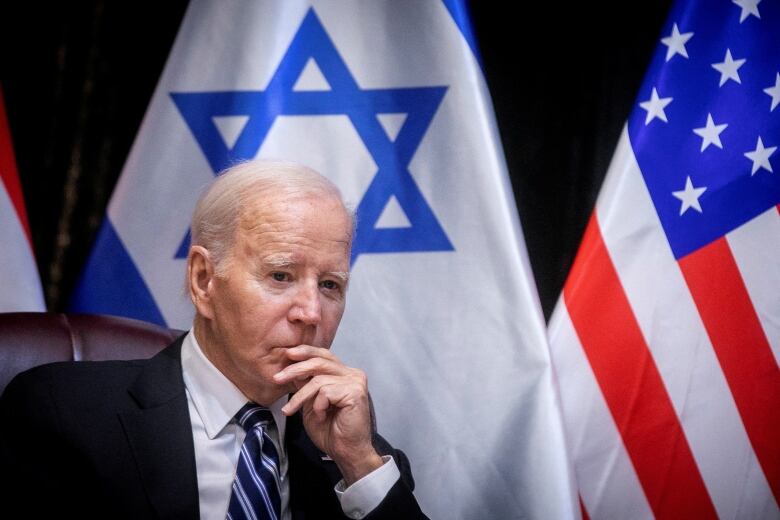 Biden with hand on chin, with Israeli and US flags behind him