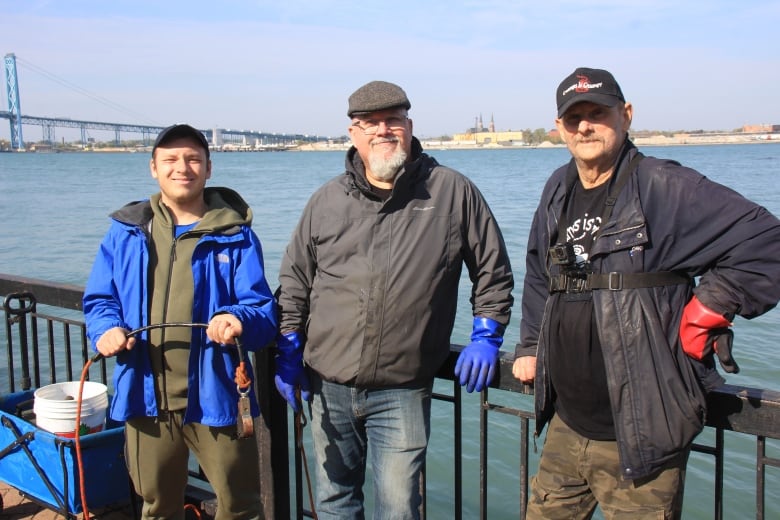 Three men stand in front of the river