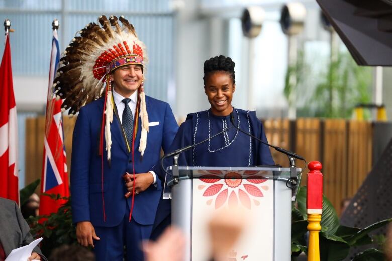 A man in a headdress and suit and a person in traditional Nigerian attire stand behind a podium.