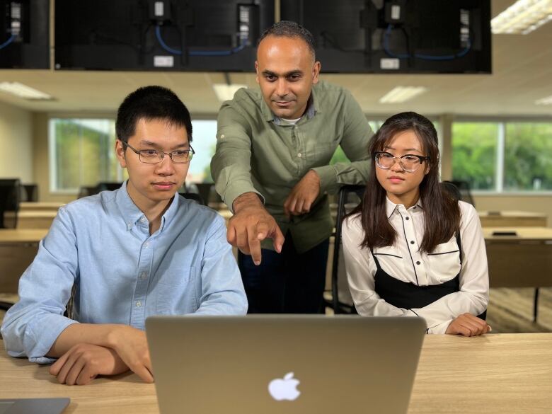 Three people huddled over one Macbook computer. 