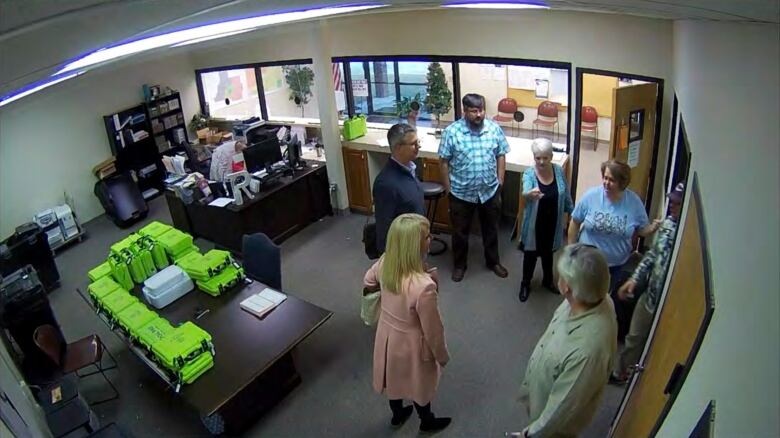 Several individuals are shown in an office setting in a video still taken from a security camera inside the room.