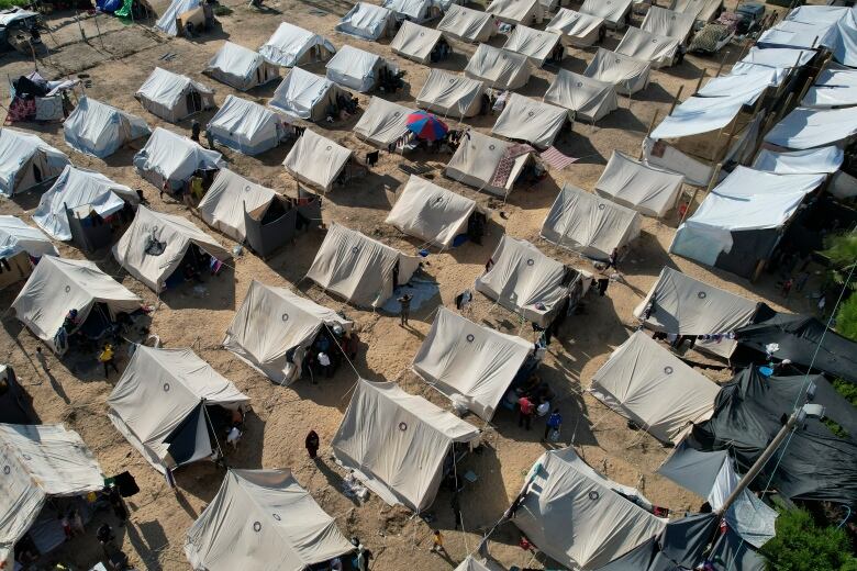 A series of white tents are shown on a ground of dirt in an overhead view.