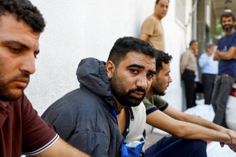 A grieving man sits on the concrete ground outside a hospital. 