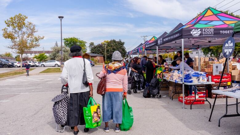 People line up to collect food from tables in a parking lot. 