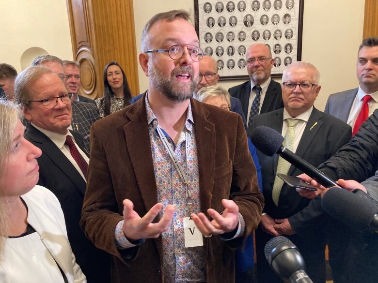 A tall man with glasses speakers in a reporter's microphone in a crowded room.