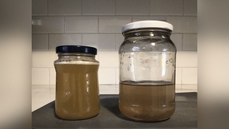 Two jars of brown water sitting on a counter.