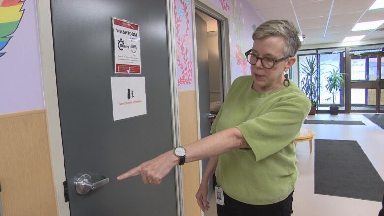 Woman is standing and pointing at a door. A sign on the door says 