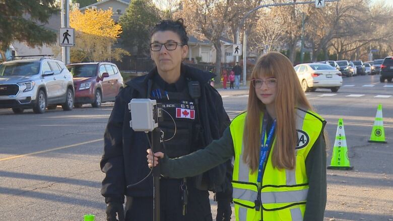 Student in yellow vets holds radar stick next to police officer.