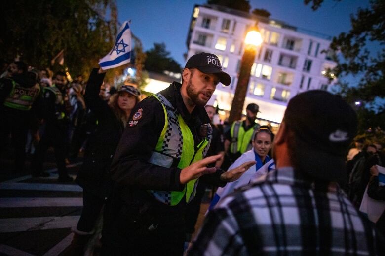 A police officer speaks to a protestors with some people holding Israeli flags behind him.