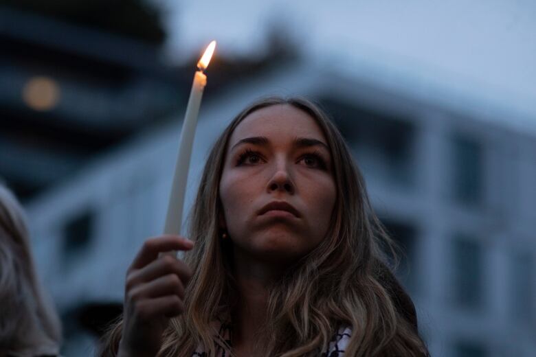 A young woman holds a candle up.