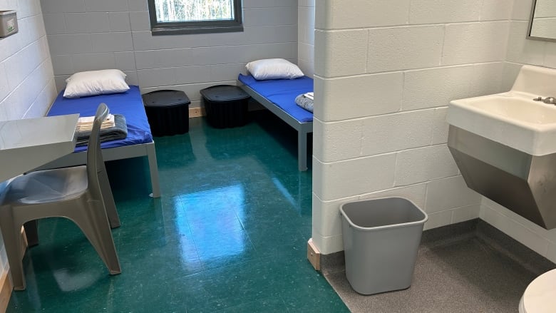 Cell with two small beds, two chairs and desks, and a sink and toilet.