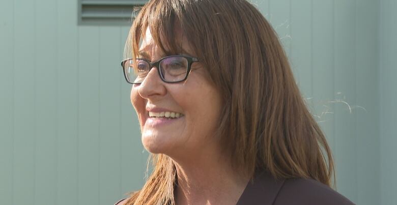 Woman with glasses and long hair smiles as she speaks outdoors.