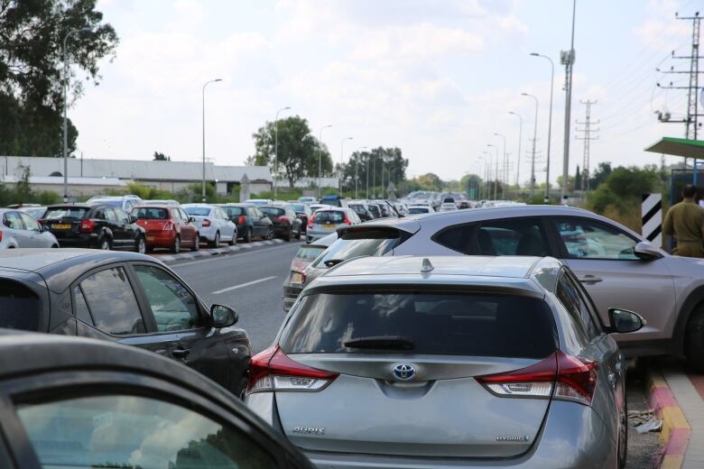 Dozens of cars are seen parked on or beside the road, some haphazardly, off into the distance.