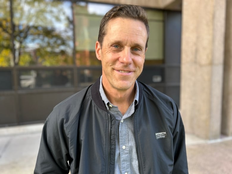 A man with short haircut standing in front of a concrete building