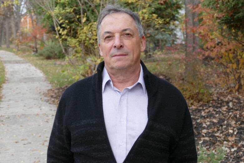 A man in a black sweater standing outside on the sidewalk. 