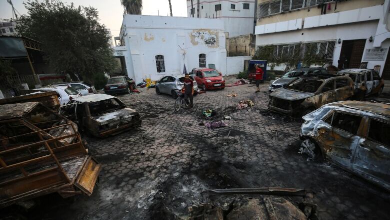 Pedestrians walk through an explosion site strewn with destroyed vehicles.