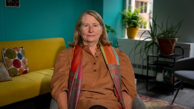 A woman in an orange shirt sits in a chair. 