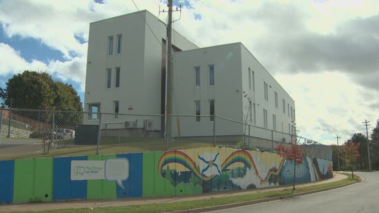 A grey building with a mural outside is shown from the street. 