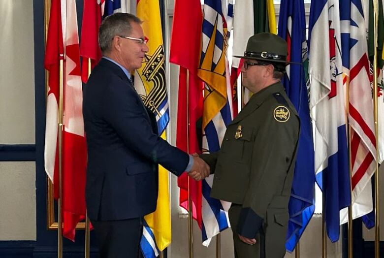 Border patrol agent in dark green uniform shakes hand with man in suit.