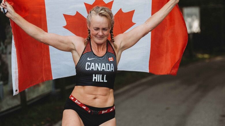 Althlete holding the Canadian flag high as she completes the race