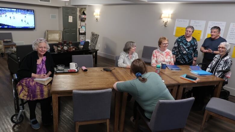 A group of older adults sit around a boardroom table in a common area.